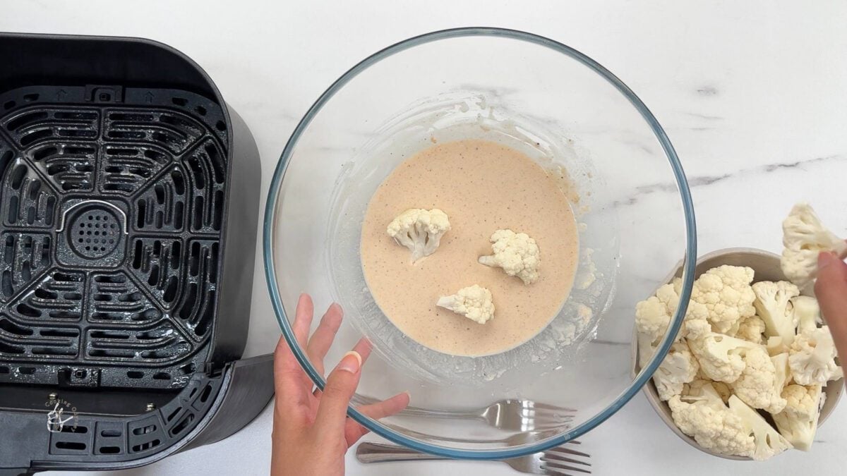 cauliflower florets added to the batter in a bowl 