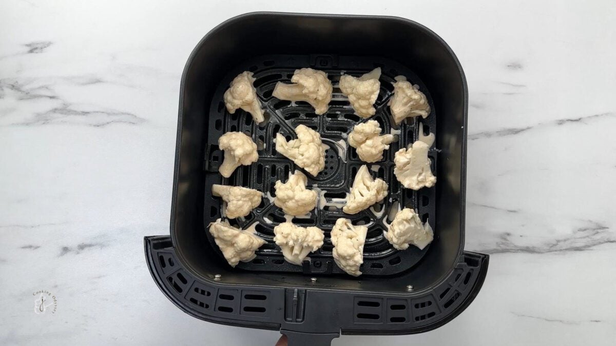 batter coated cauliflower florets placed in the air fryer basket