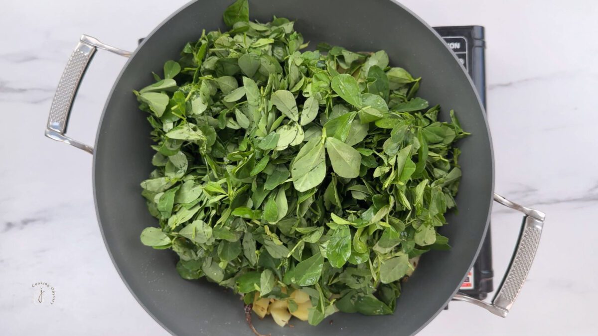 fresh roughly torned fenugreek leaves added to the half cooked potatoes in the pan for aloo methi recipe