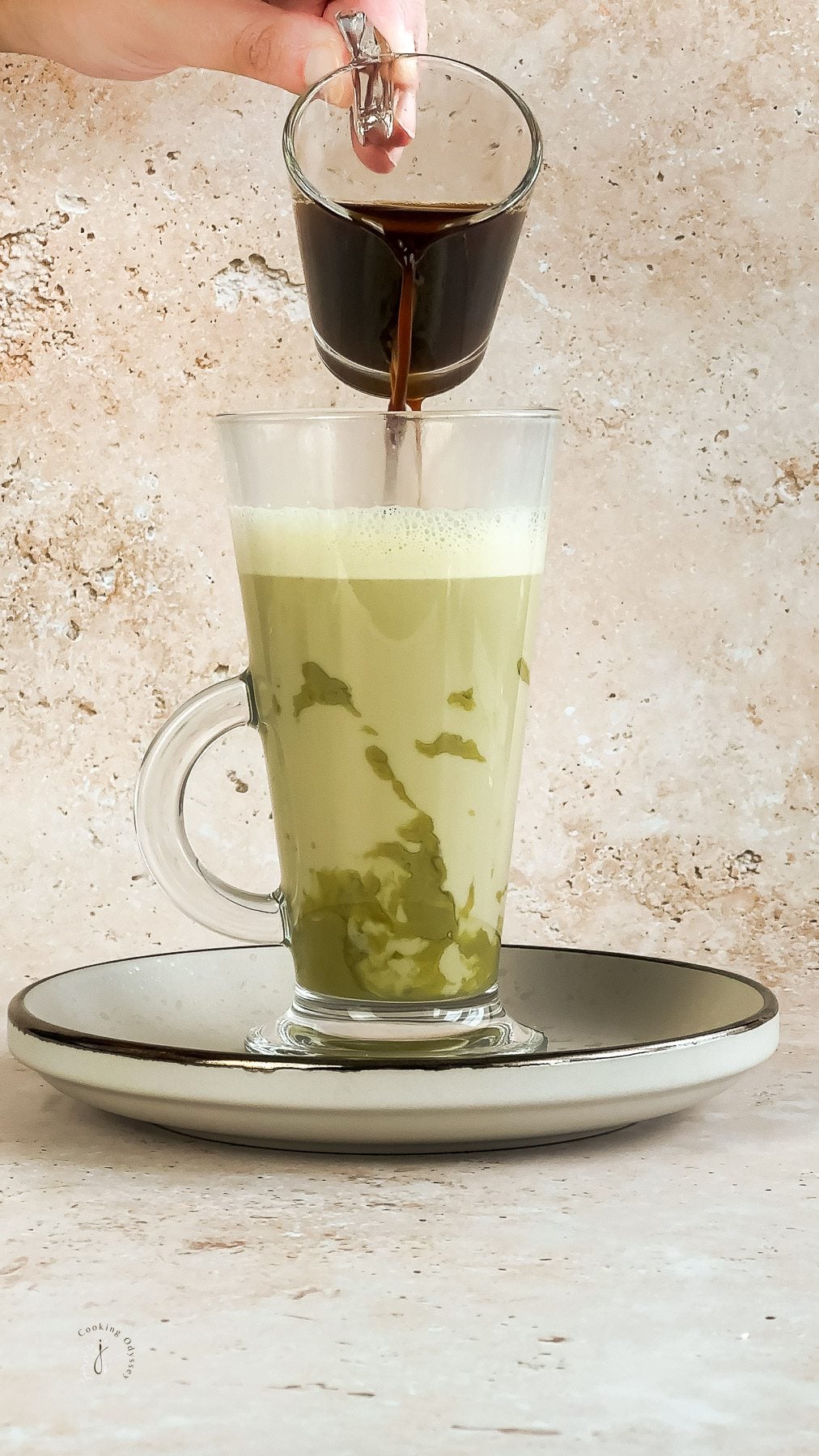 A female hand is pouring espresso shot in to the frothy milk to create strabucks style pistchio latte