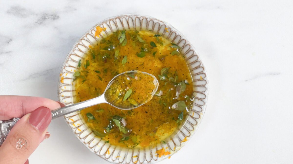 a female hand is mixing a oil dressing using a spoon