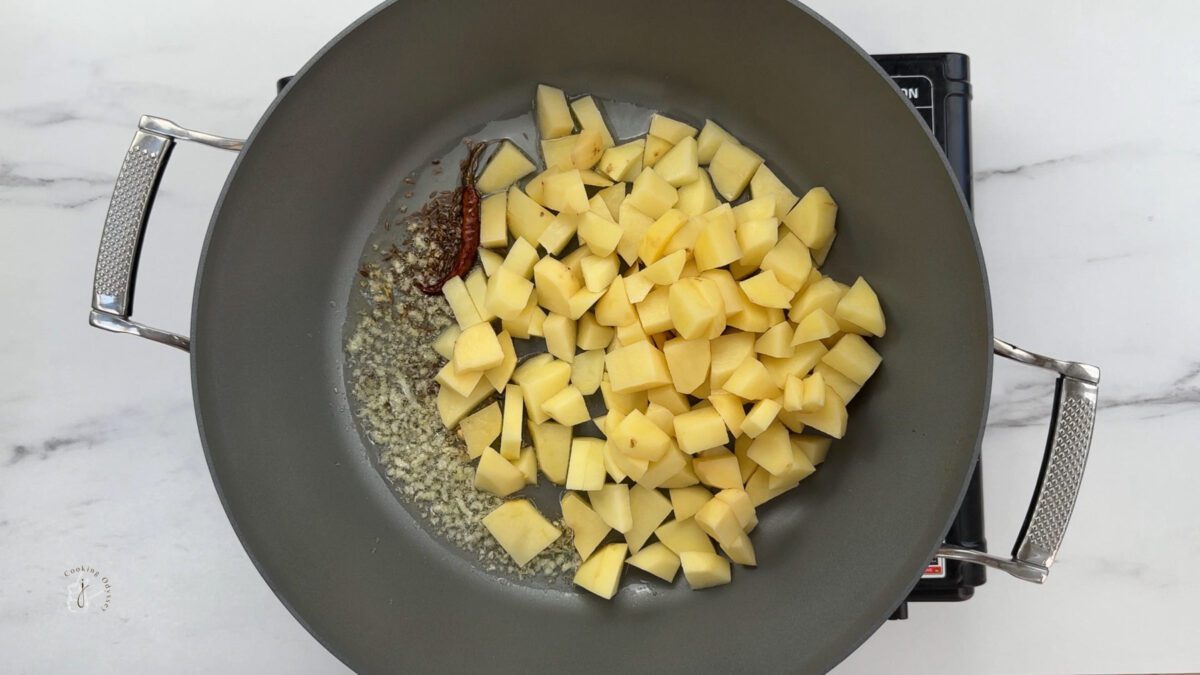 chopped potatoes added to the garlic tadka in the pan to make methi aloo