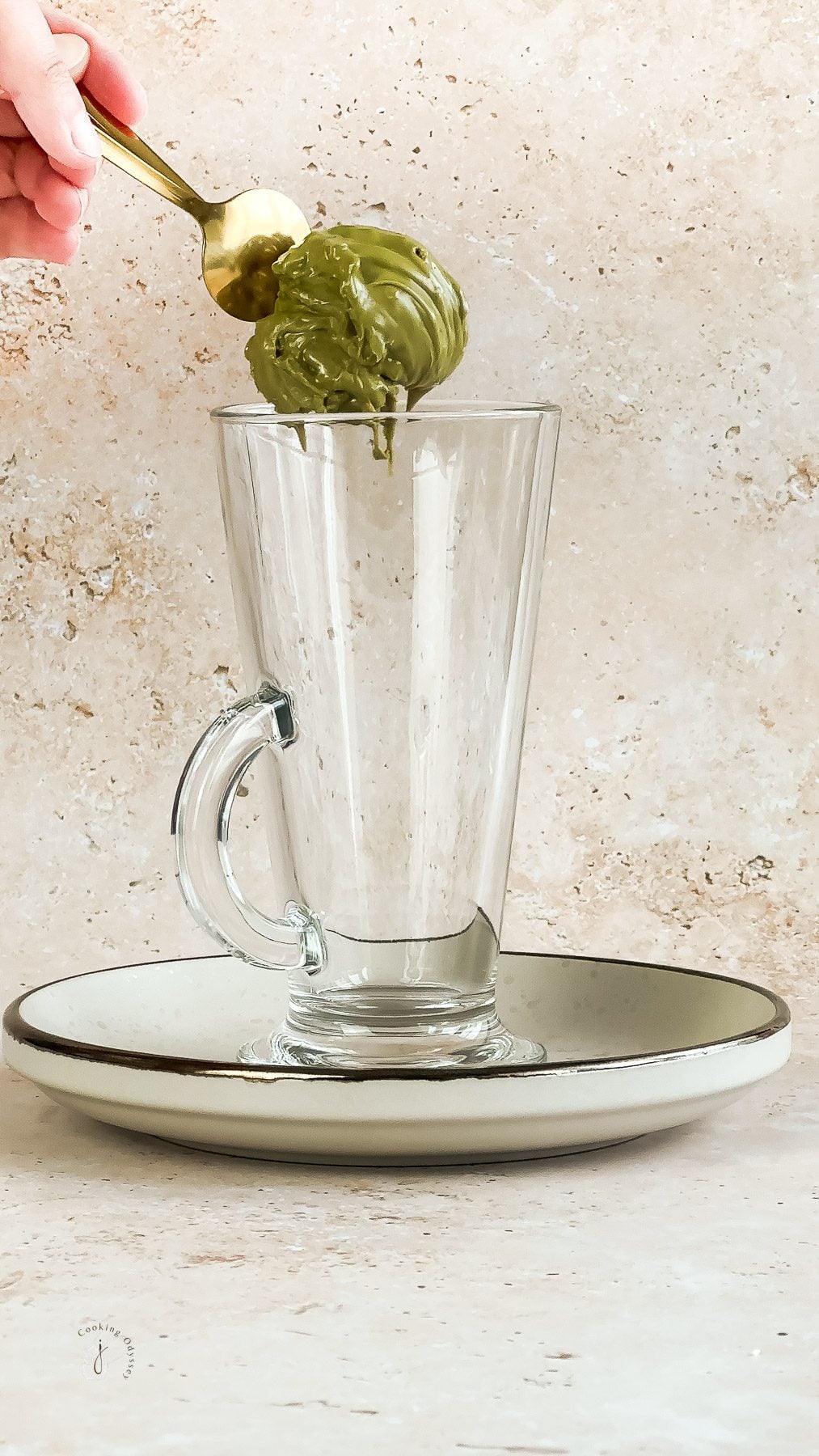 A female hand is spooning pistachio cream in to the latte glass