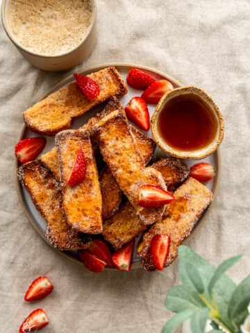 air fryer french toast sticks in a plate next to coofee cup on a breakfast table
