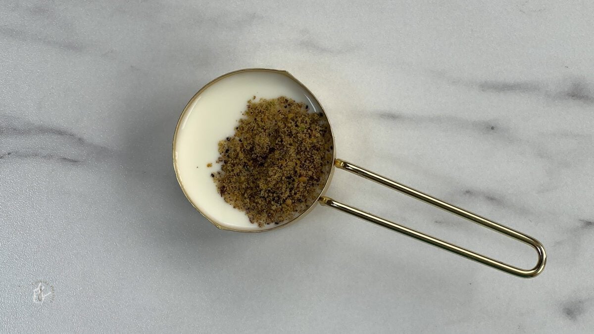 ground pistachio and cardamom added to the milk in a small bowl