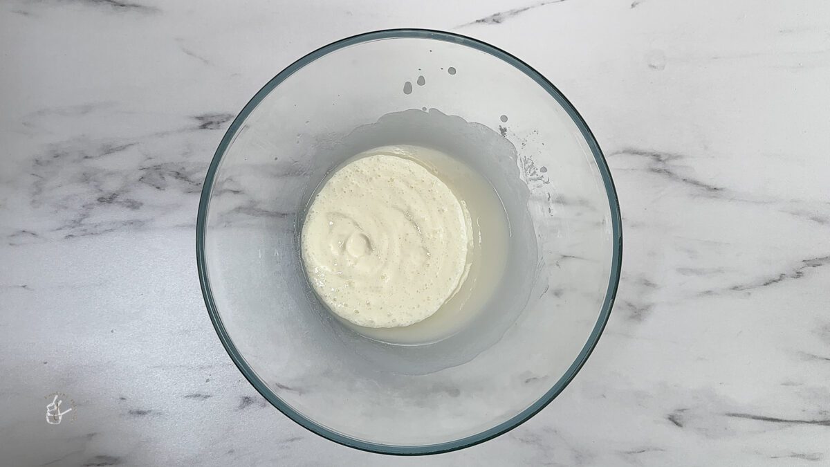 Frothy yogurt added to the sugar and oil mix in a bowl
