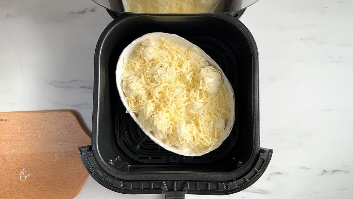 A baking dish filled with cauliflower cheese placed in the air fryer basket to cook