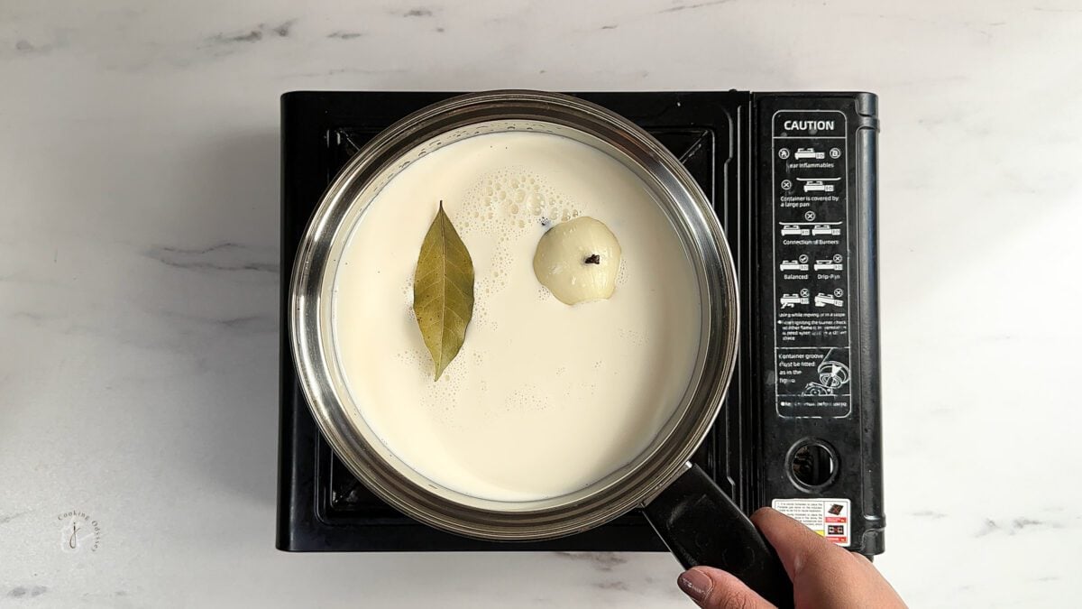 milk, onion and whole spices in the pan to make air fryer cauliflower cheese