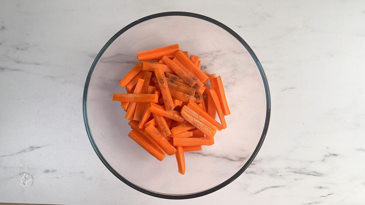 raw carrot sticks mixed with seasoning and oil in a clear bowl