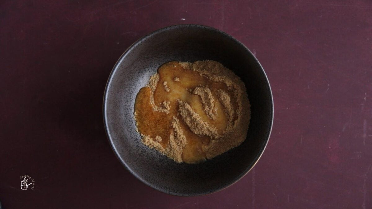melted butter added to the crushed biscuits in a black mixing bowl