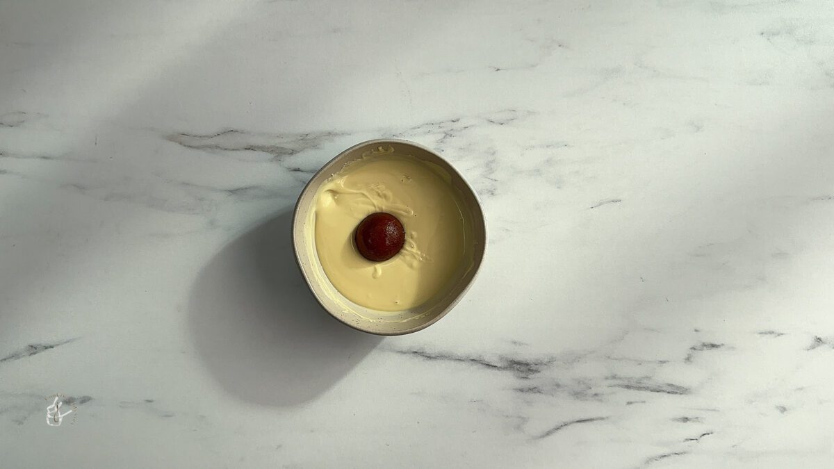 one gulab jamun placed in melted white chocolate in a bowl