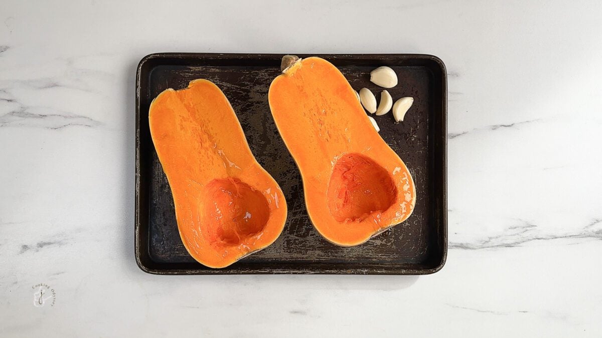 two halves of butternut squash on a baking tray next to garlic cloves