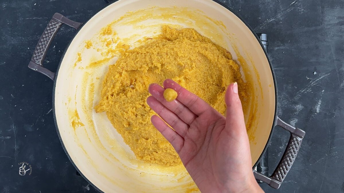 a female hand is showing a small piece of kesar badam katli dough