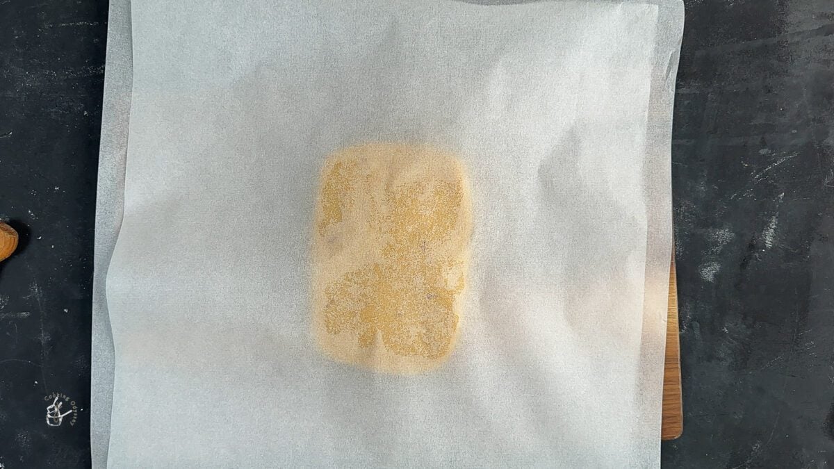 katli dough placed on greaseproof paper and another paper placed on top of the dough