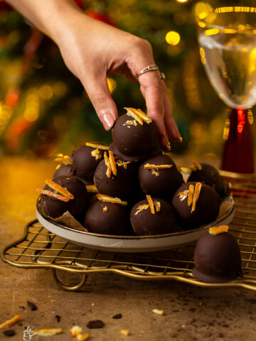 A female hand is putting a christmas truffle on other truffles that are on the plate.