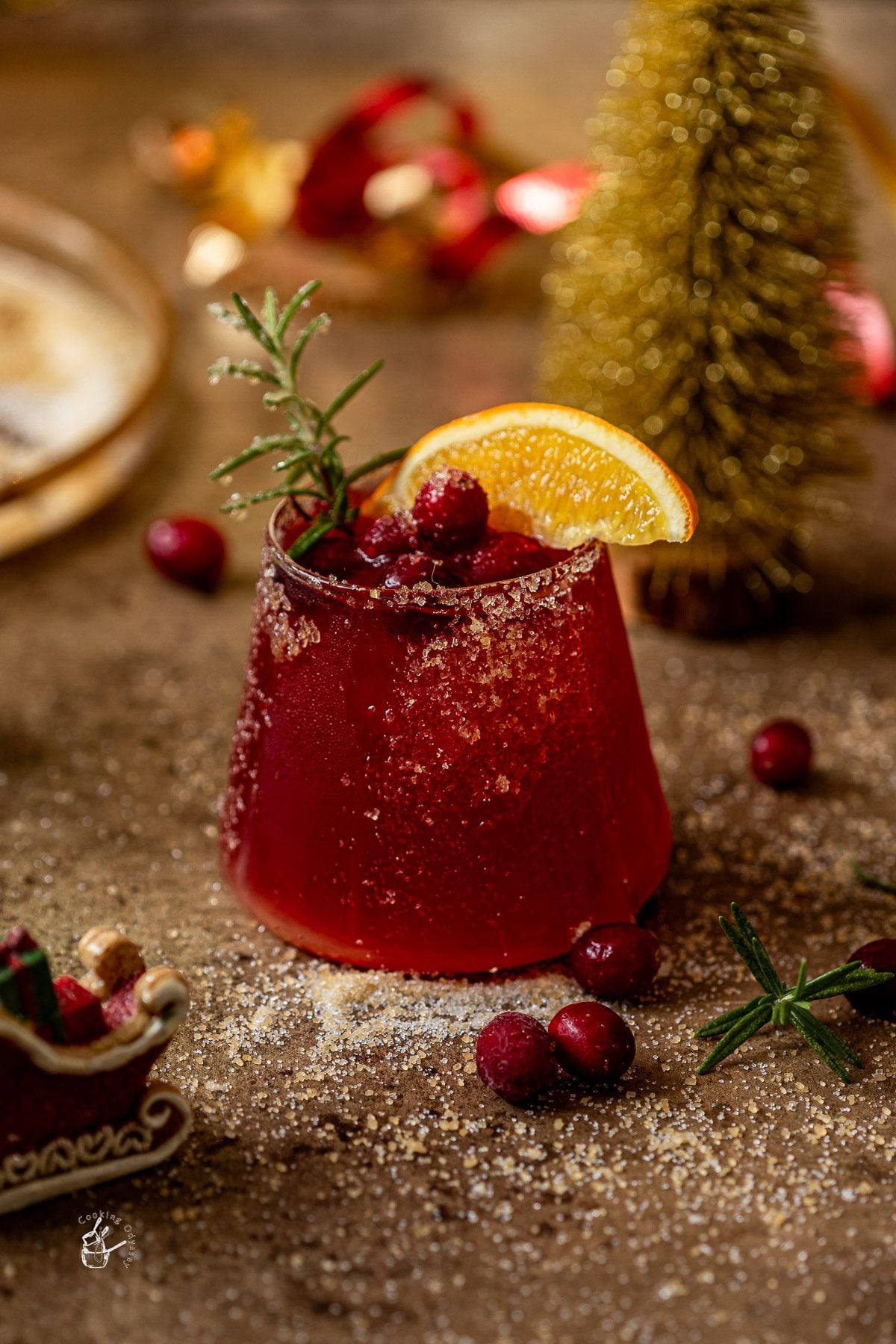 cranberry mocktail recipe glass placed on a brown backdrop that is garnished with fresh cranberries, orange wedge and rosemary sprig
