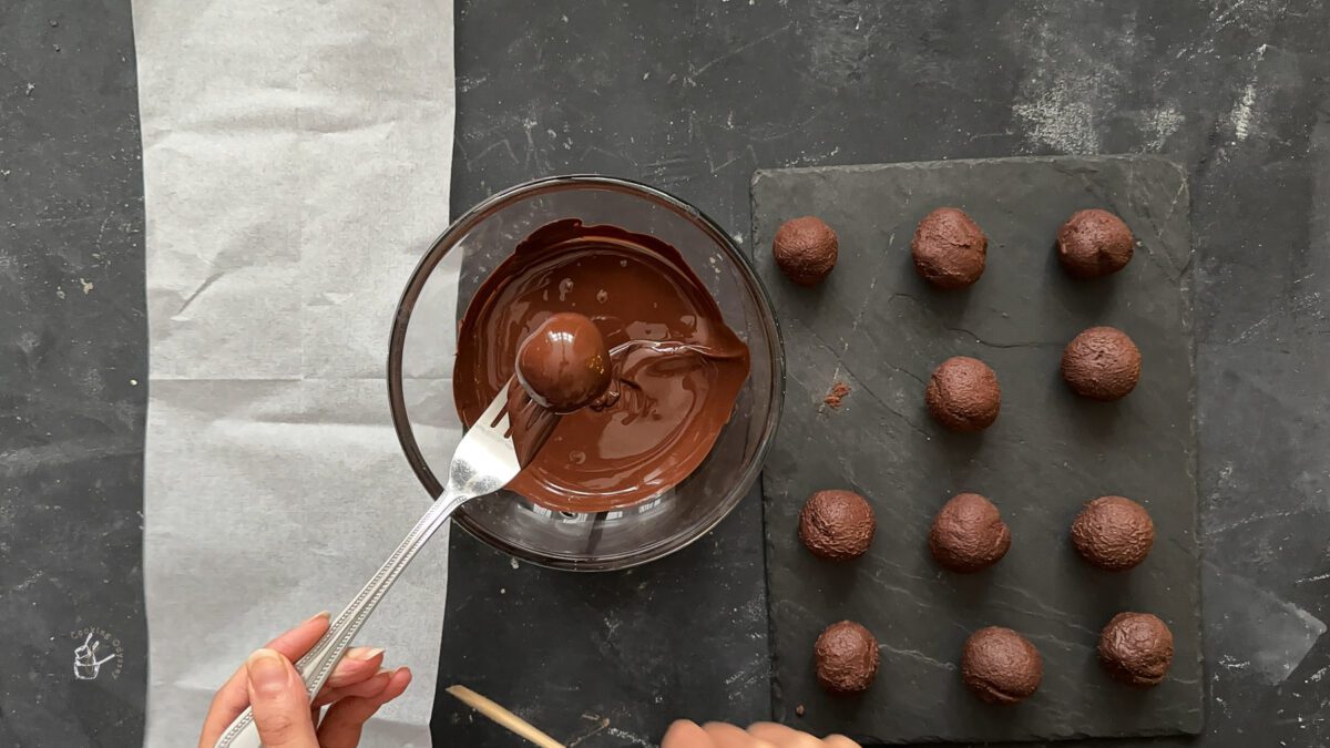 a female hand is dipping a christmas truffle in melted chocolate using a fork. 