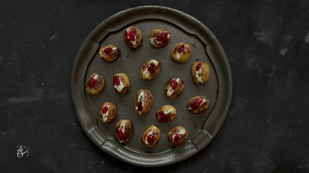 small baked potatoes in oven are on the plate topped with feta dip and cranberry sauce.
