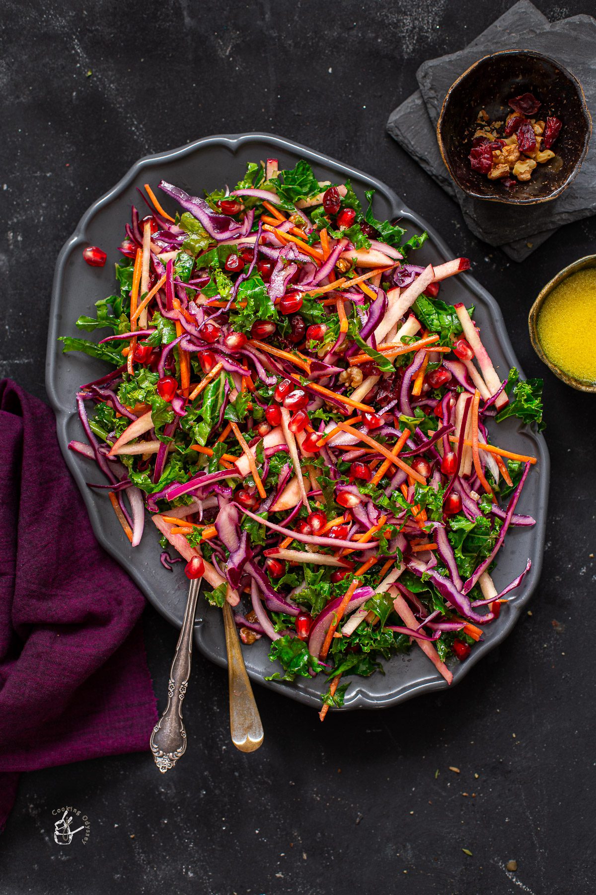 winter slaw in a oval serving plate next to two small bowls of cranberries and dressing.
