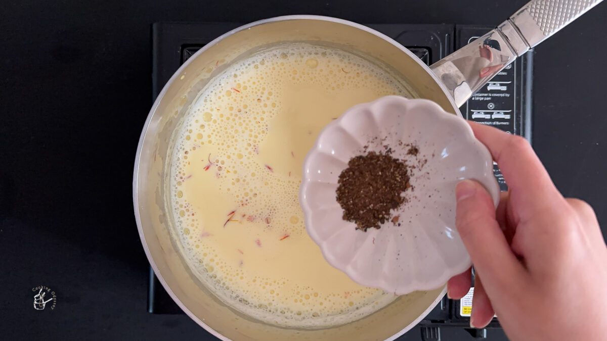 a female hand is adding cardamom powder to the indian kesar milk. 