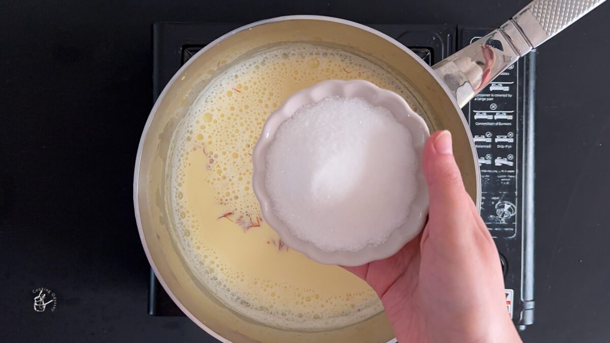 a female hand is adding sugar in the kesar doodh in a pan. 