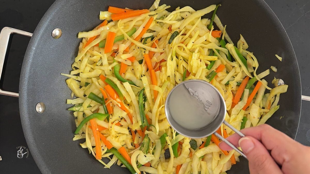 a female hand is pouring lemon juice in a cooked gujarati kobij no sambharo.