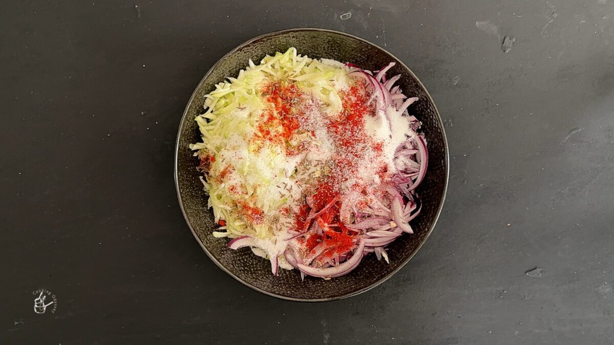 sugar and spices added to the raw mango and onions in a bowl.