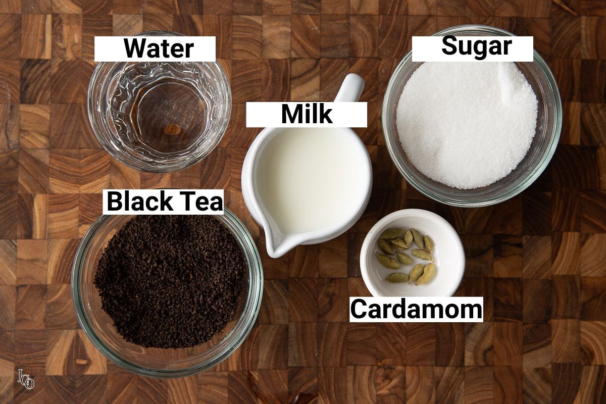 Cardamom chai ingredients arranged and labeled - milk, cardamom pods, sugar, water and loose black tea leaves.