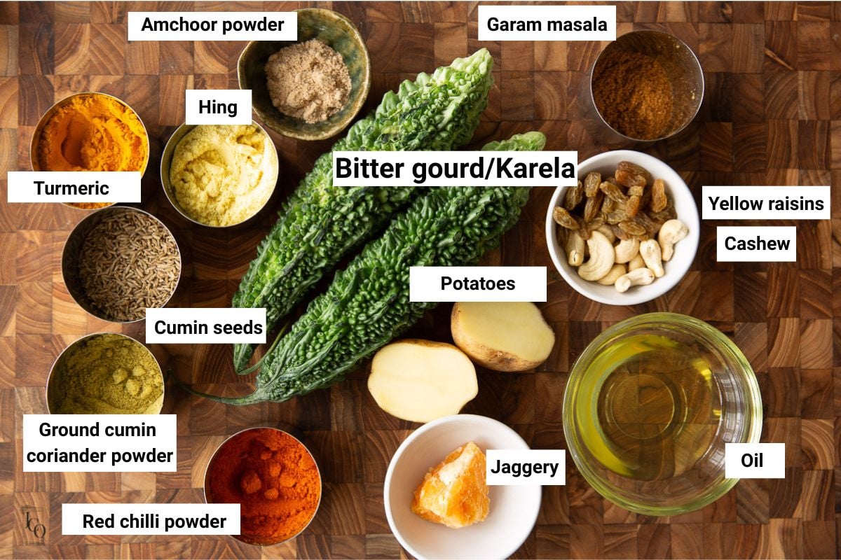 Bitter gourds, spices, oil, jaggery and amchoor powder in small bowls.