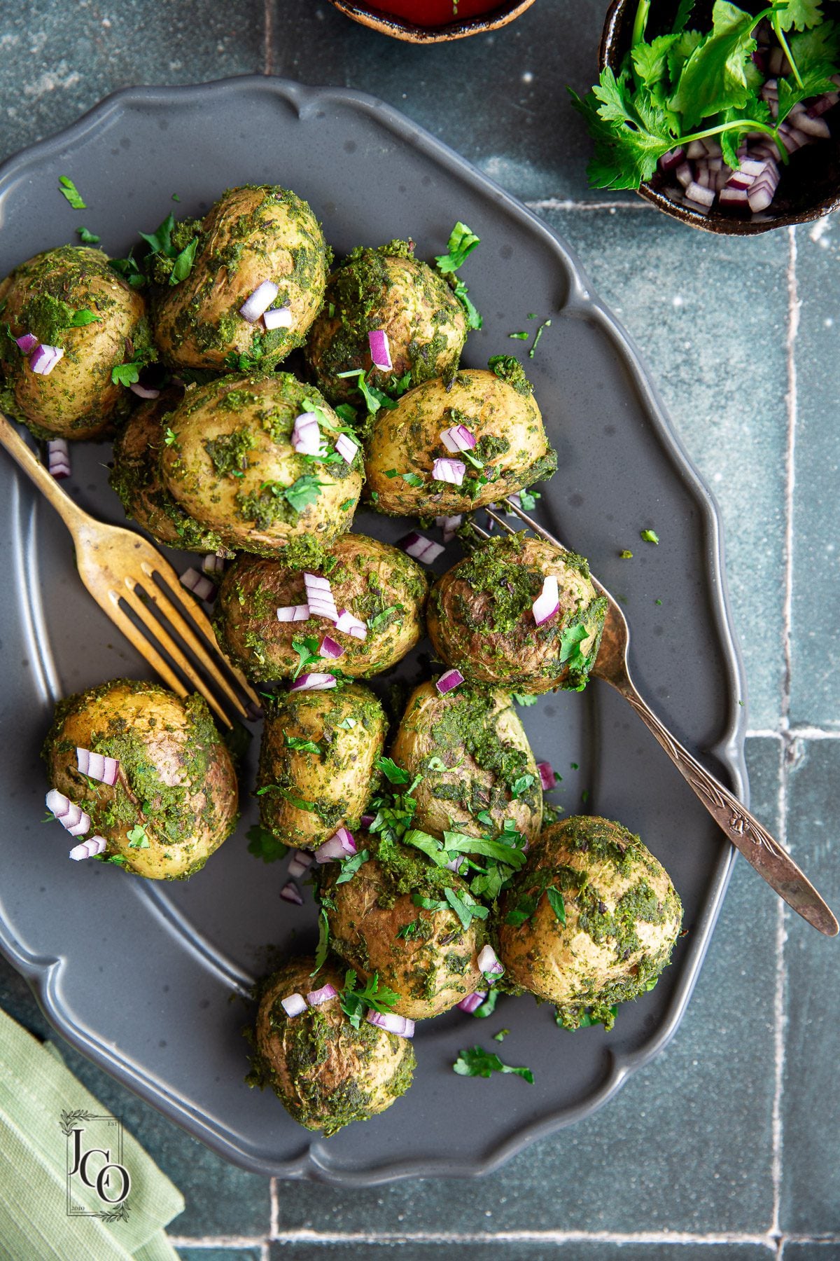 Baby potatoes coated in green chutney on the dark grey plate.