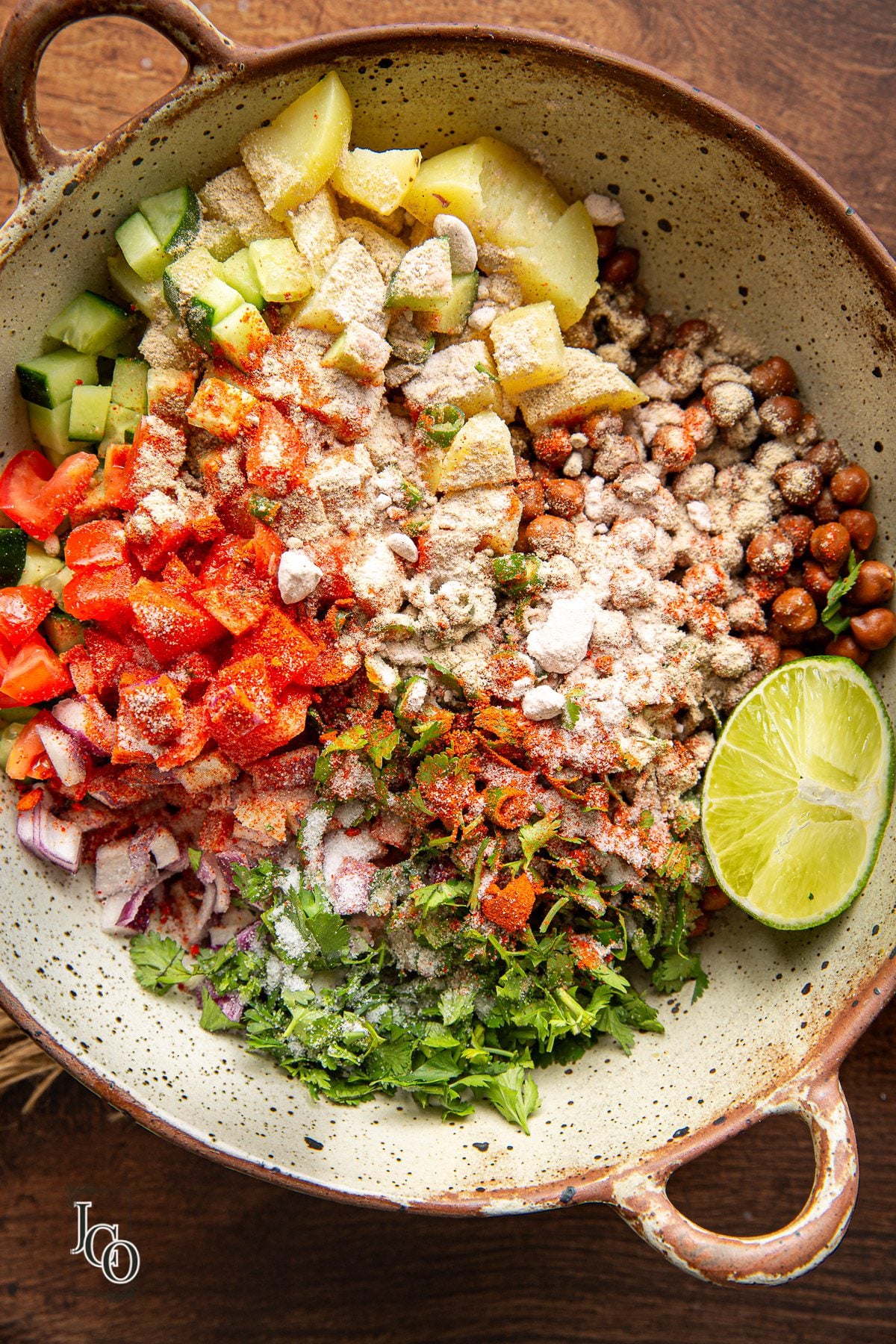 Spices powders sprinkled on boiled kala chana and chopped vegetables in a big mixing bowl.