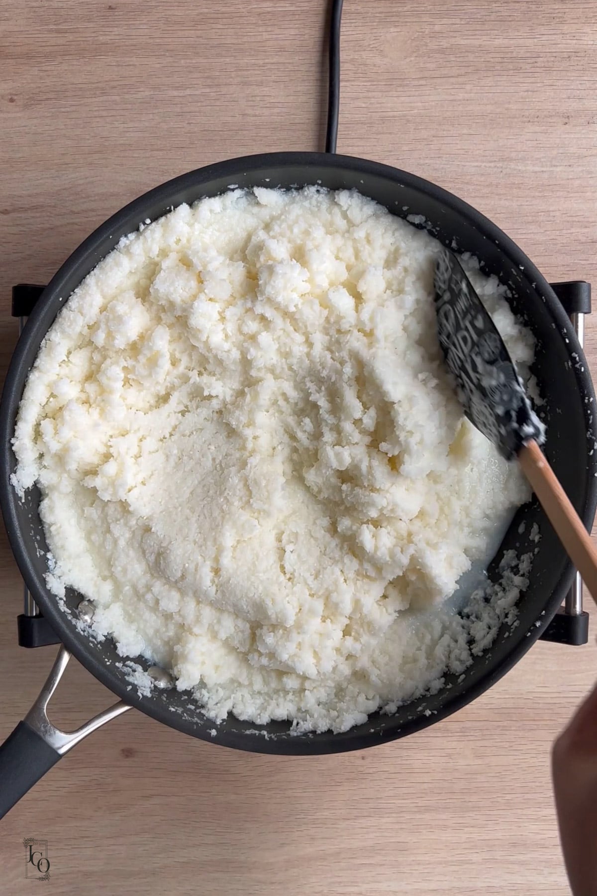 A female hand is stirring coconut mixture using a spatula. 