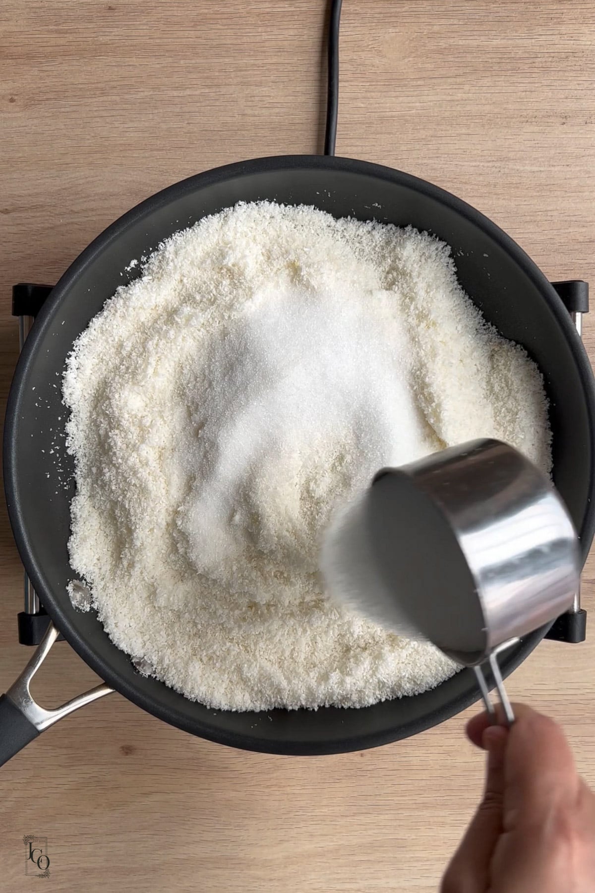 Sugar being added to the coconut in the pan. 
