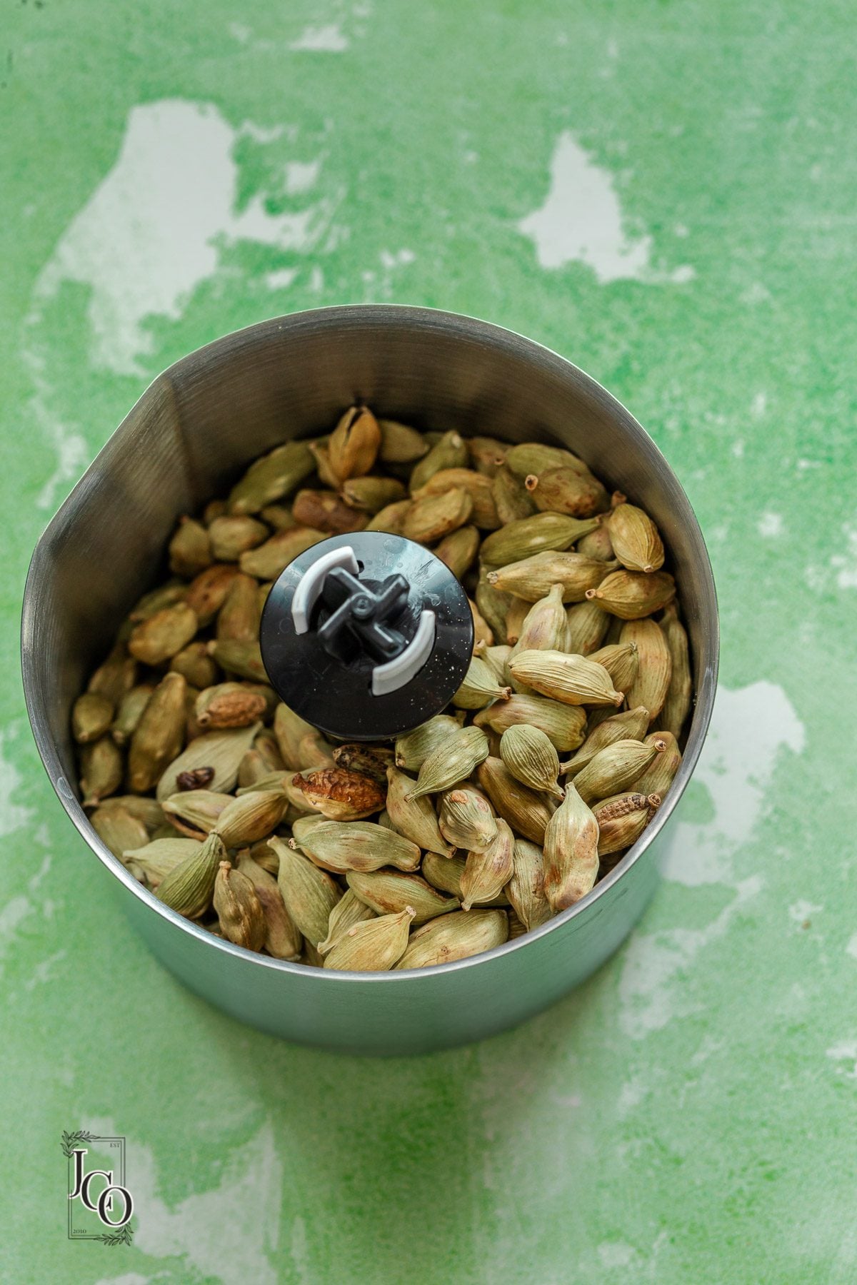 Whole lightly toasted cardamom pods in a spice grinder jar.