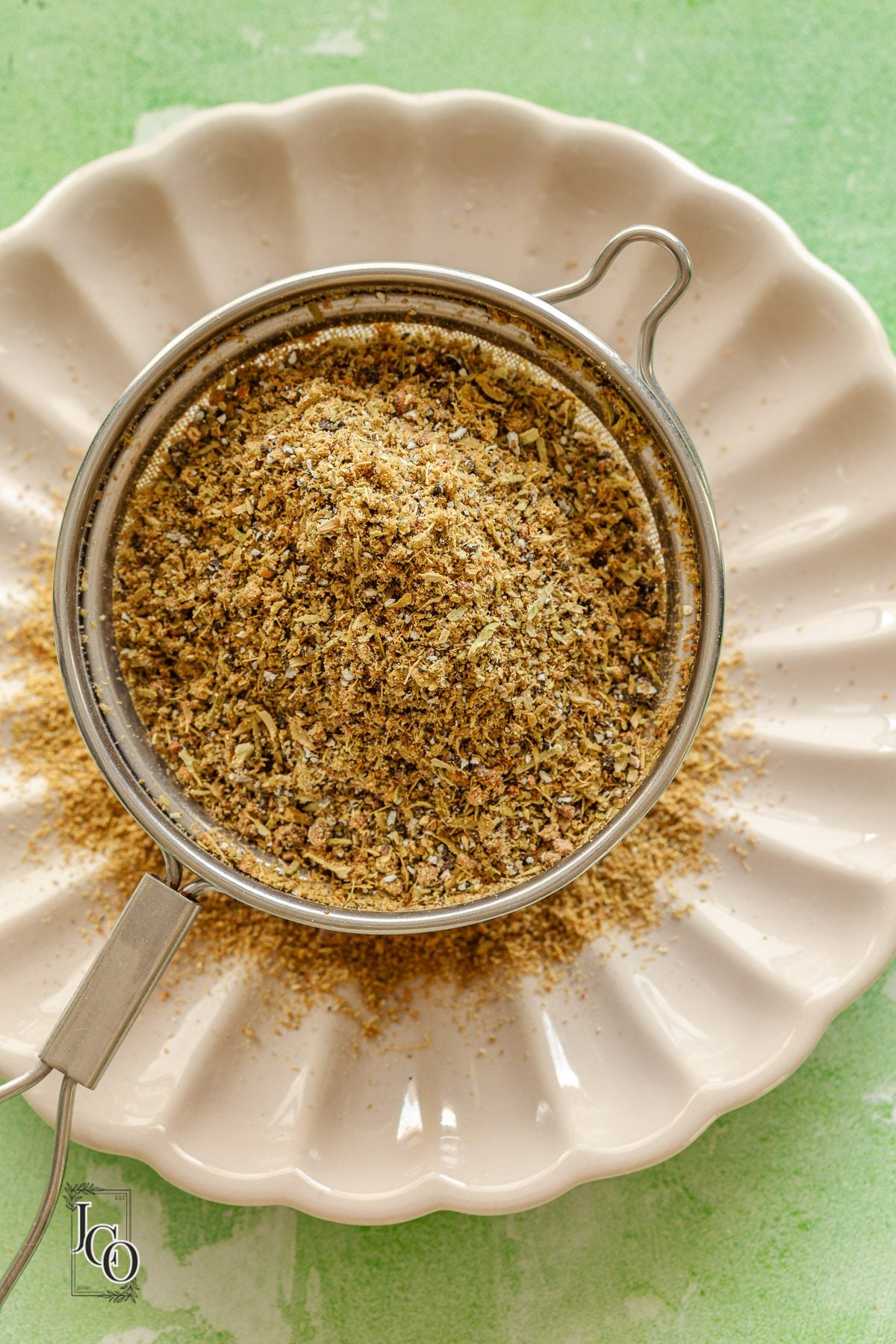 Ground cardamom powder in a fine mesh sieve on the white plate.