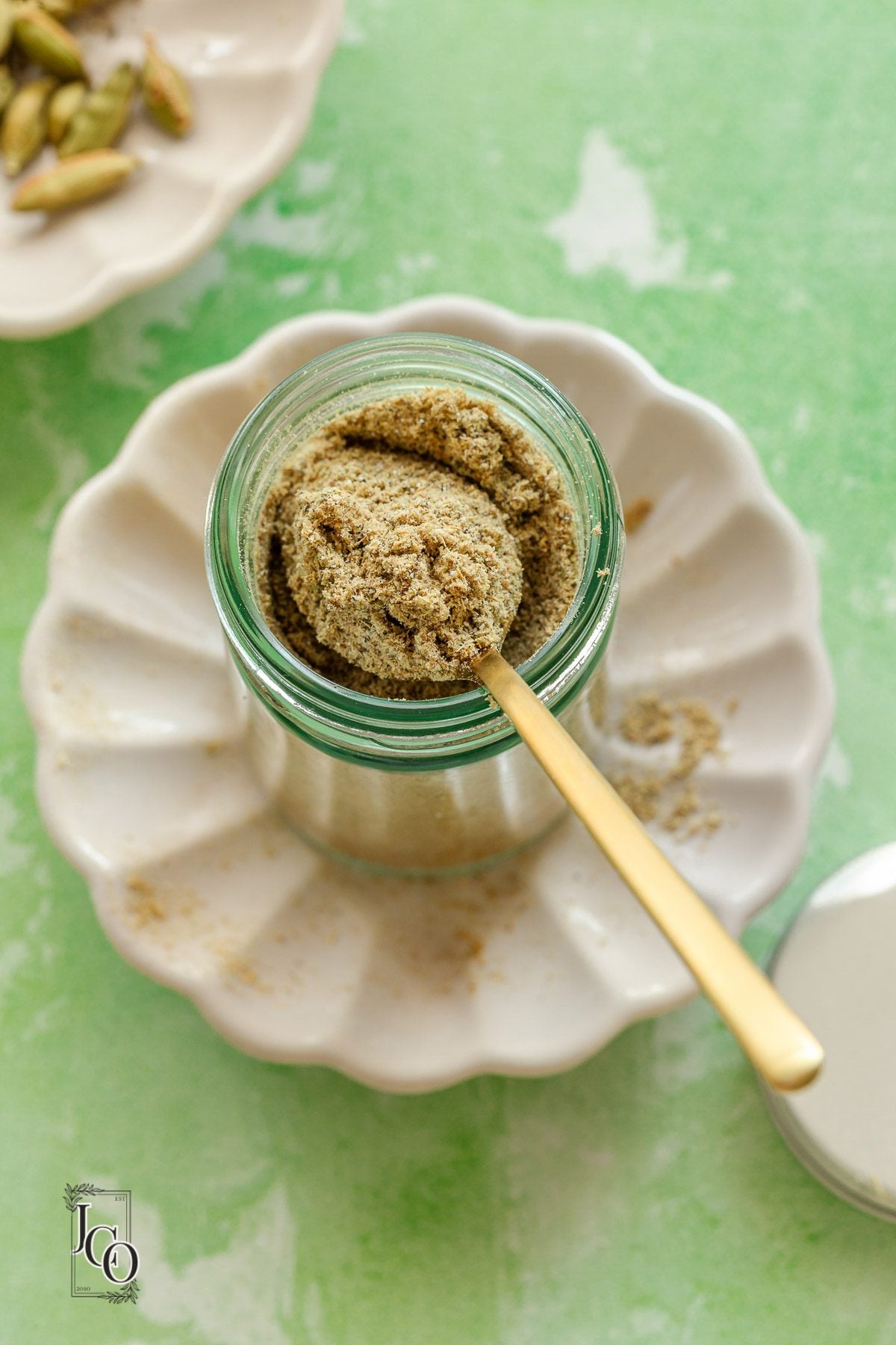 Cardamom powder in a small glass jar, next to jar lid.