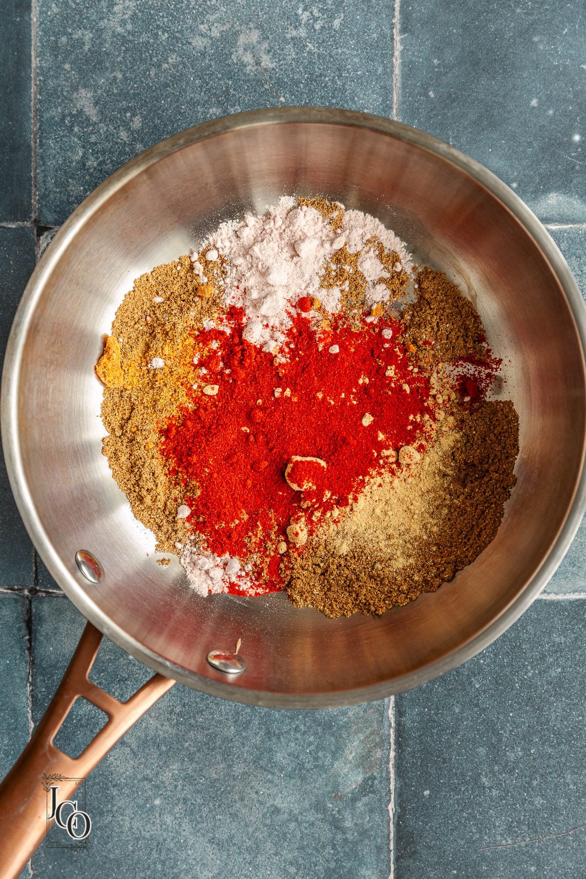 Spice powders added to the freshly ground spices in a pan.