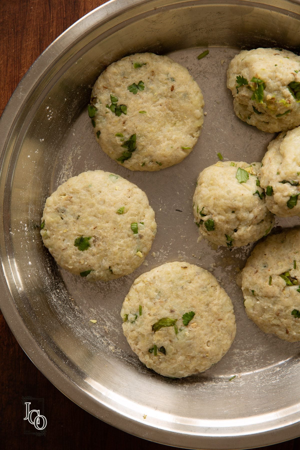 Uncooked small round flatten balls of spicy potatoes arranged on a plate.