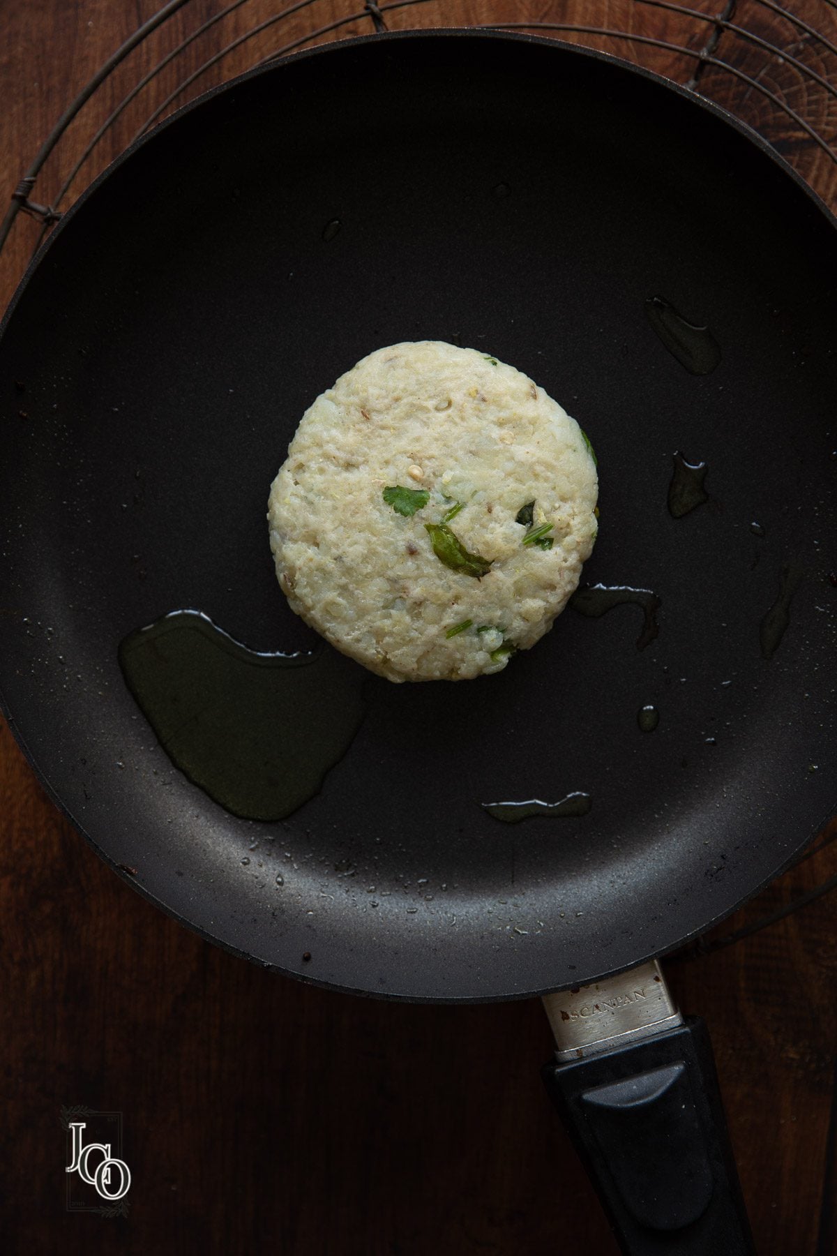 One uncooked aloo tikki placed on hot oil in a frying pan.