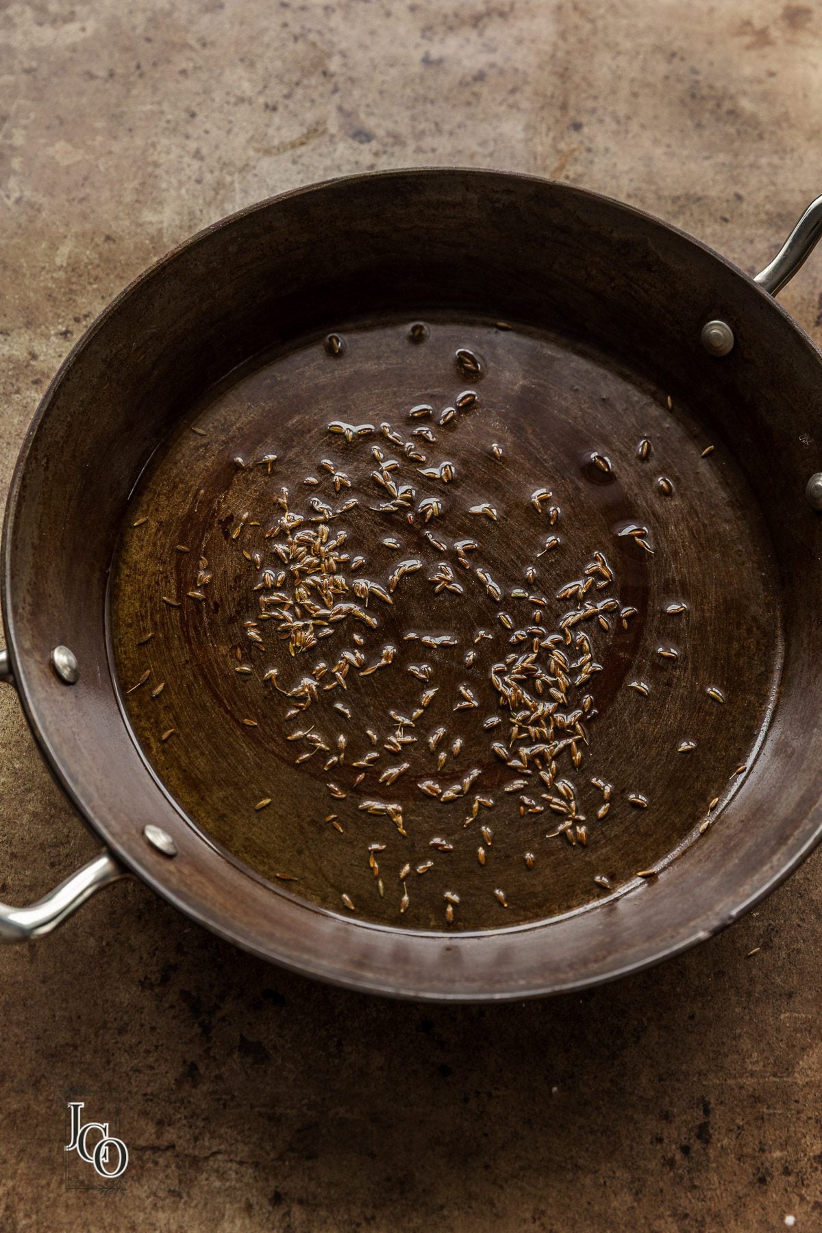 Cumin seeds added to the hot oil in a frying pan.