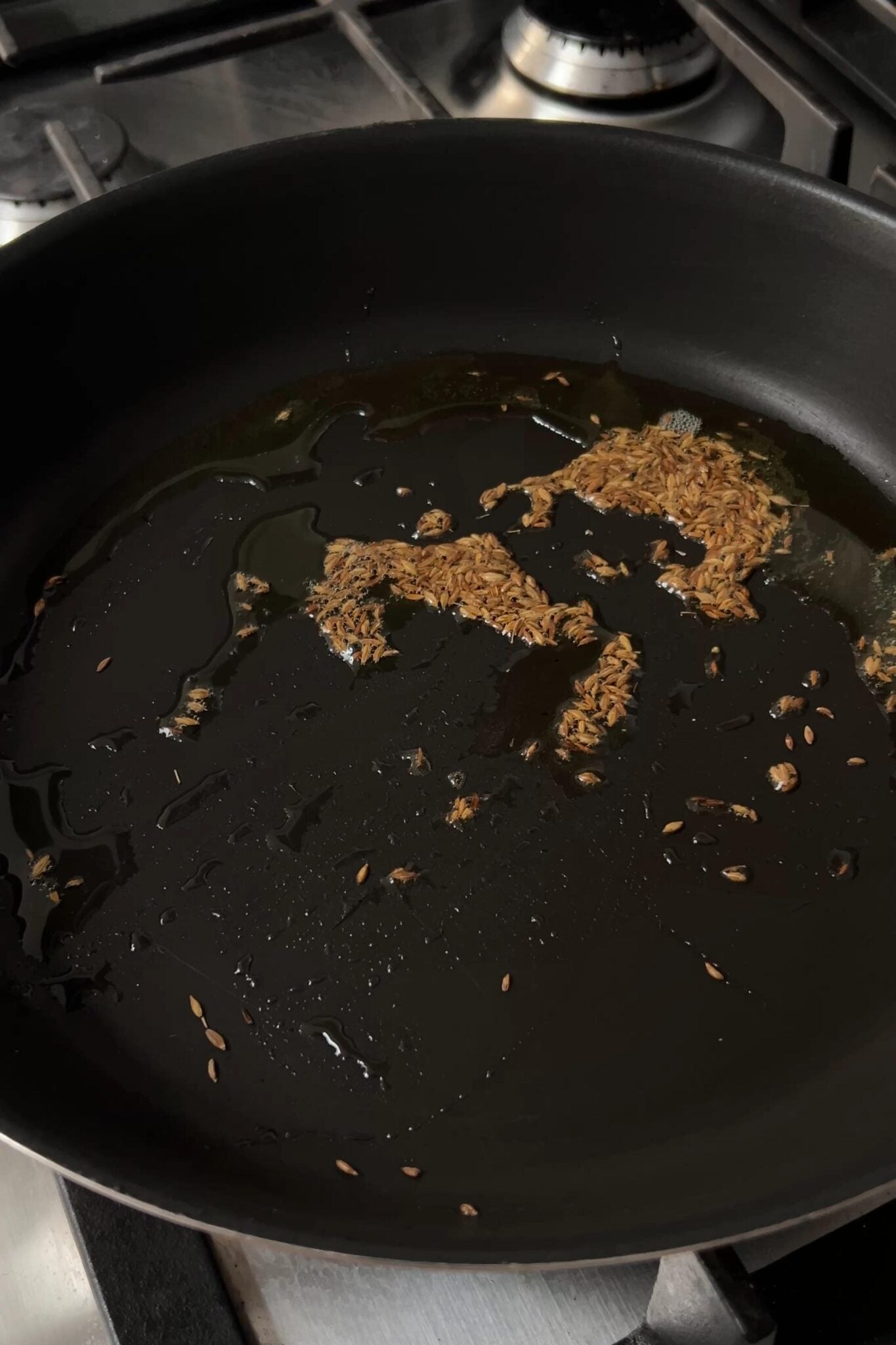 Cumin seeds sizzling in hot oil in a black frying pan.