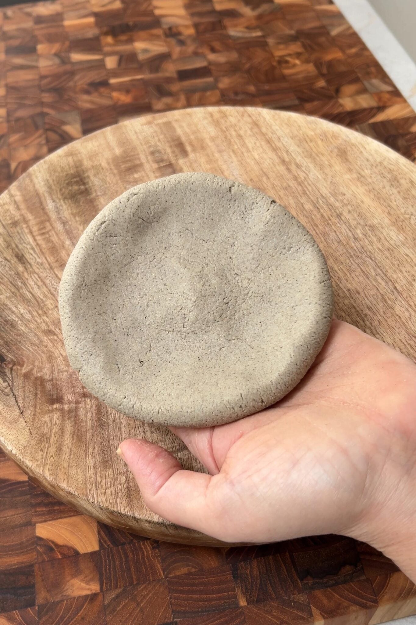 A female is showing a round disk of millet flour dough in her palm.
