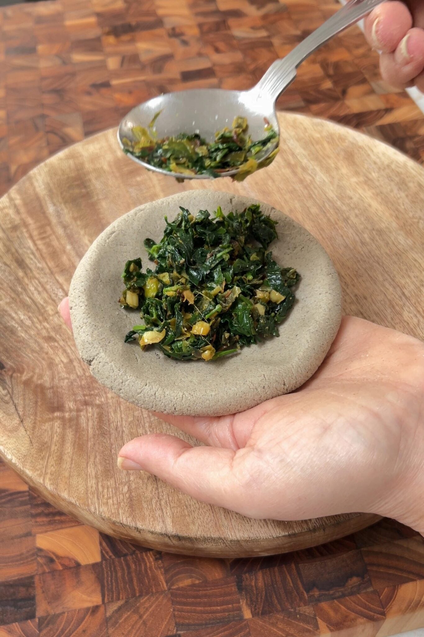 A spoon full of green stuffing placed on a small round disk of dough.
