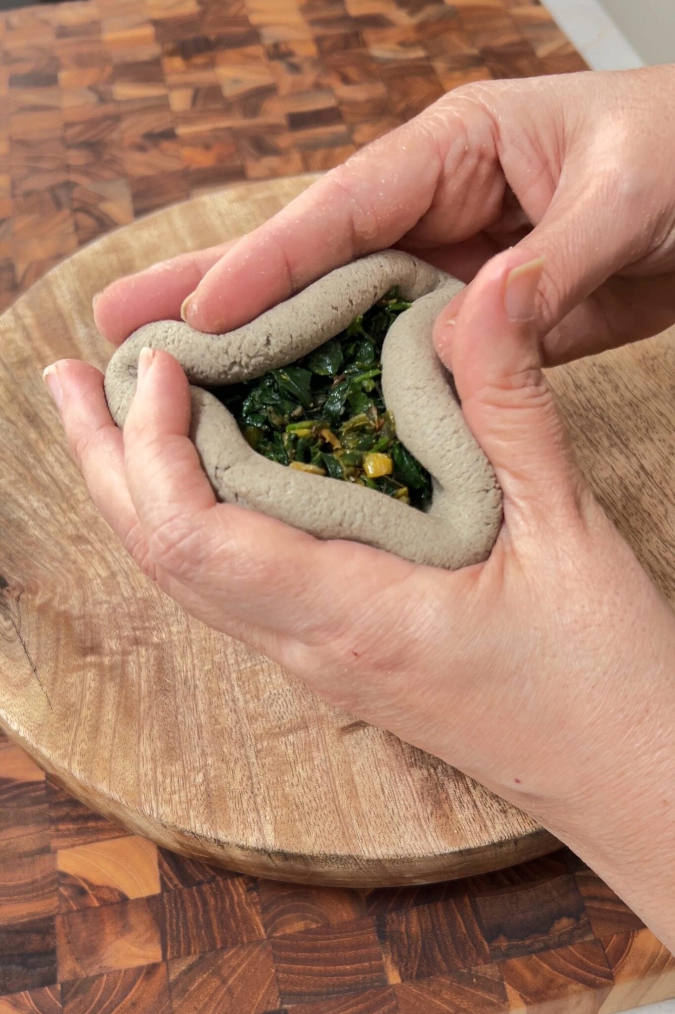 A female hand's fingers pinching the edges of the dough to seal and enclosing the stuffing.