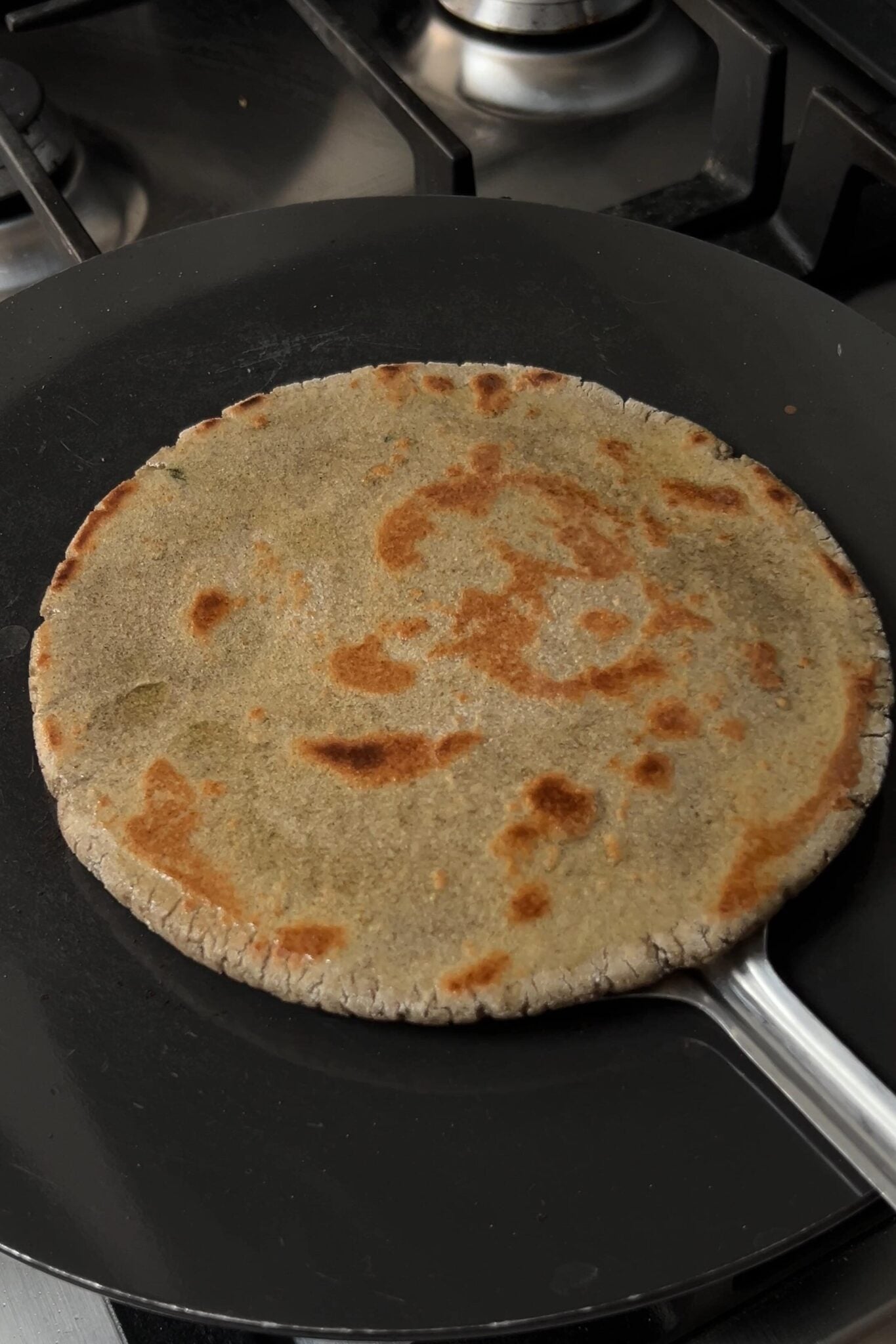 Cooked bajra rotlo is beling removed from the hot pan using a flat spatula.