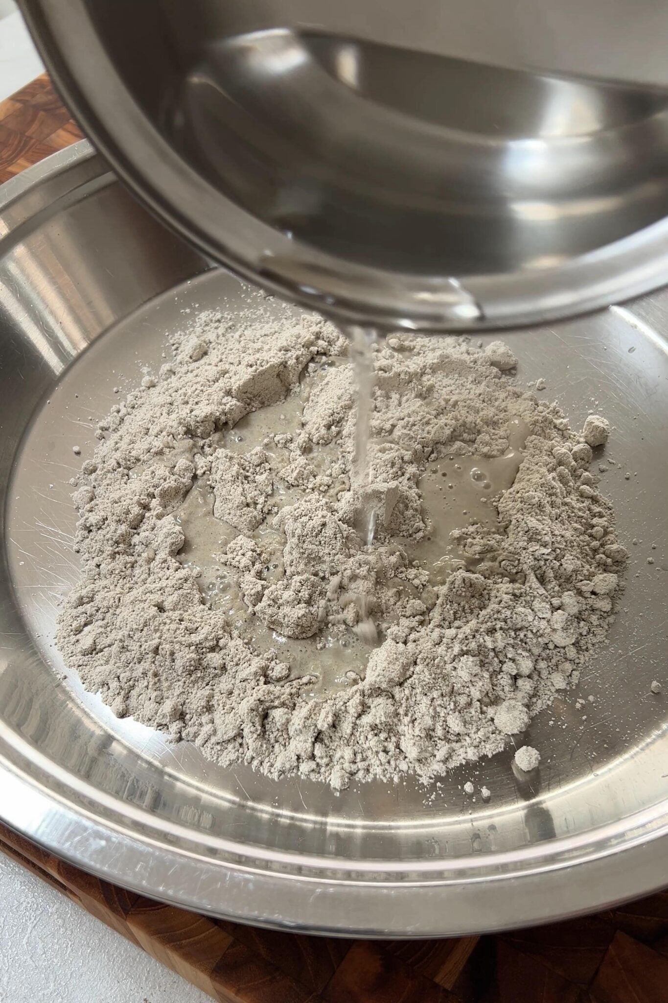Warm water is being added from the pan in bajri flour in the plate.