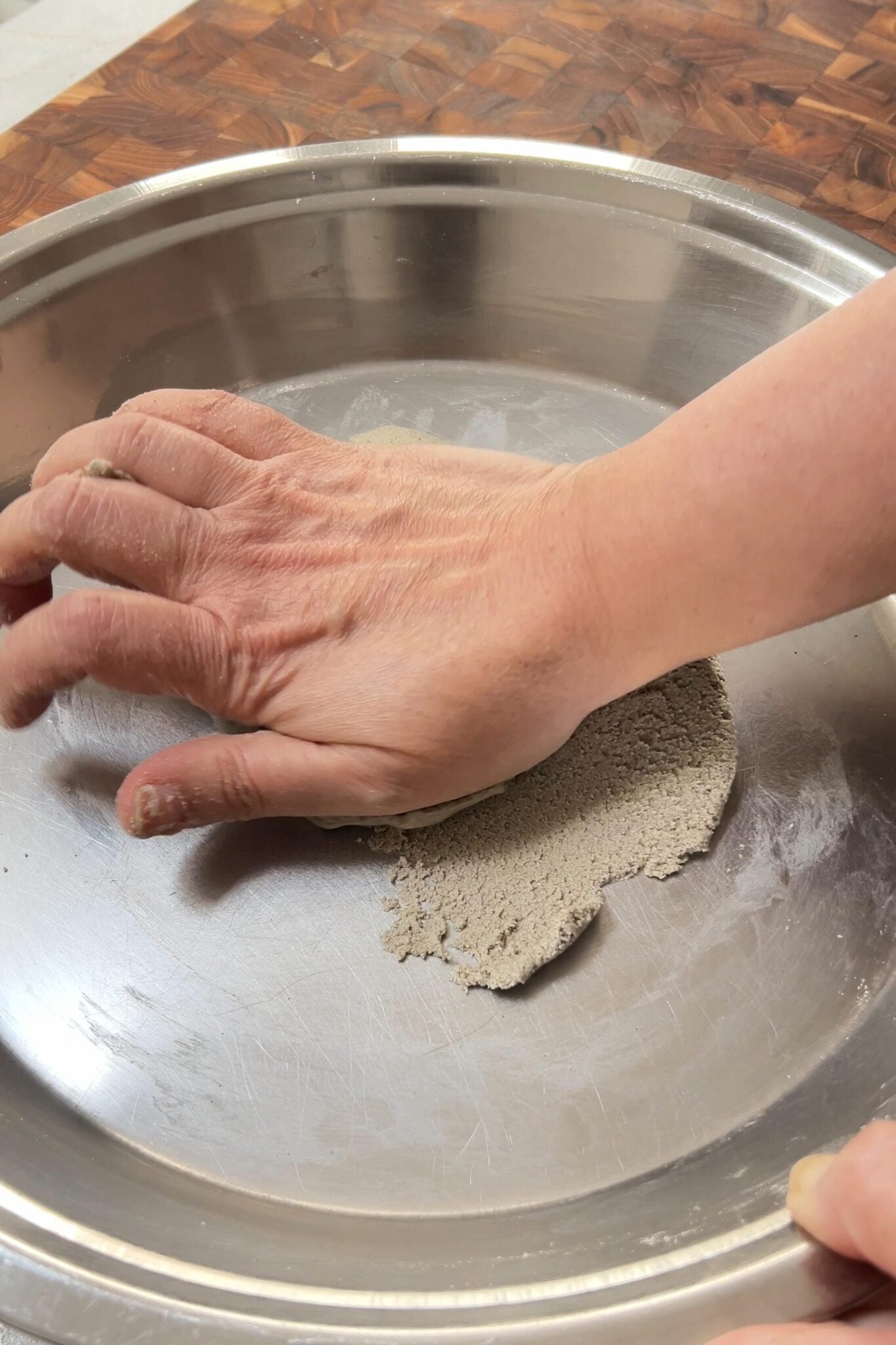 A female hand is kneading millet flour dough using a heel of her hand.