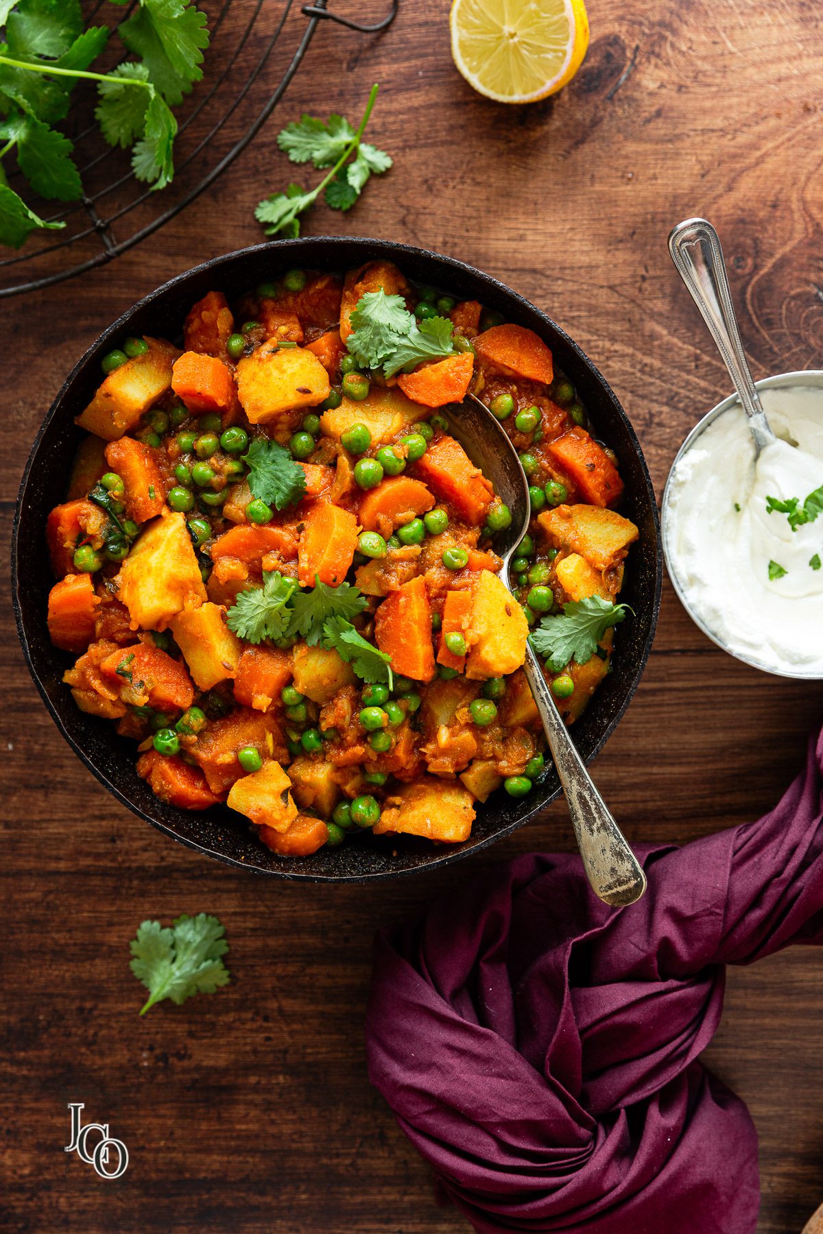 Indian curry made with potatoes, carrots and green peas served with a spoon.
