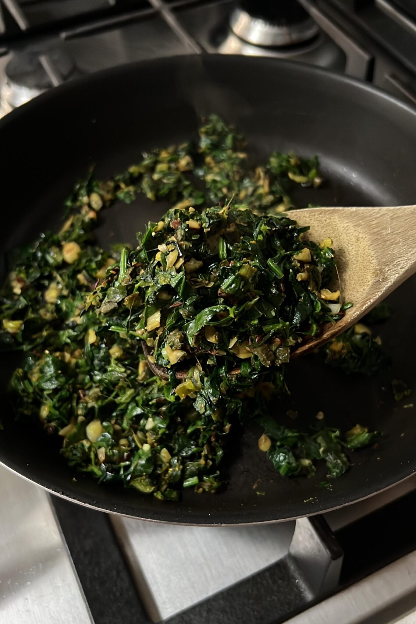 Cooked greens in a pan with a wooden spoon.