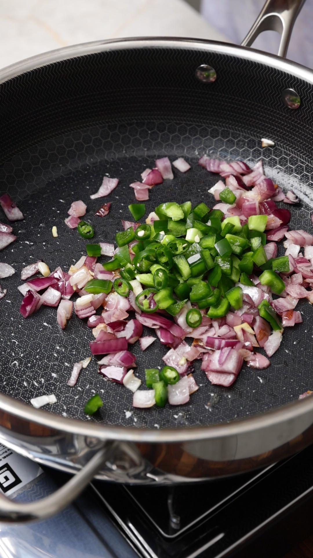 Roughly chopped green bell pepper and green chillies added to the cooked onions in a pan.